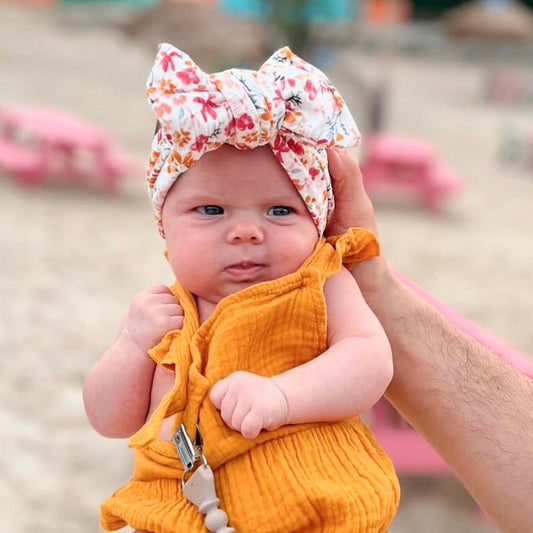 Top knot baby headband in pink floral print, crafted from ribbed knit fabric, displayed on a white background