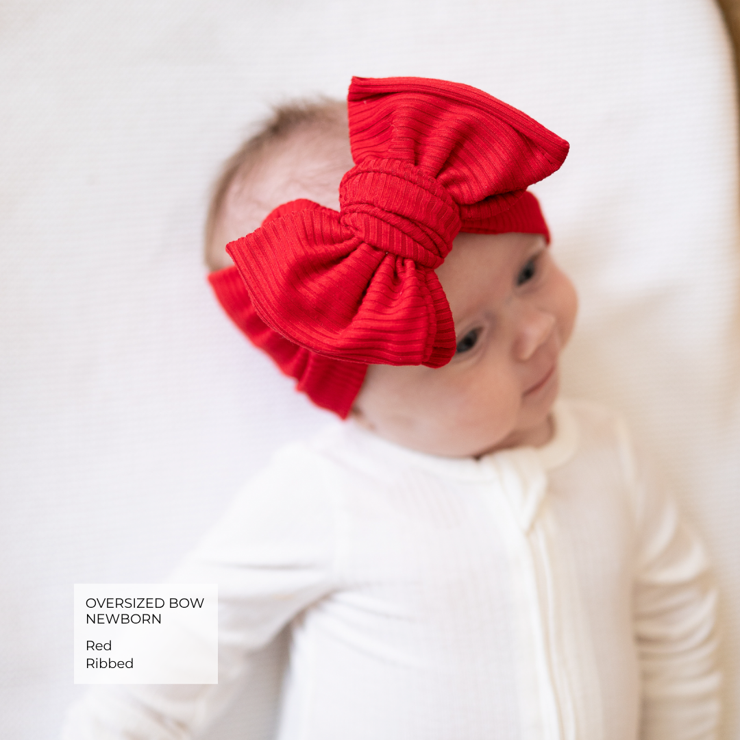 Baby wearing red ribbed oversized bow and white pajamas.