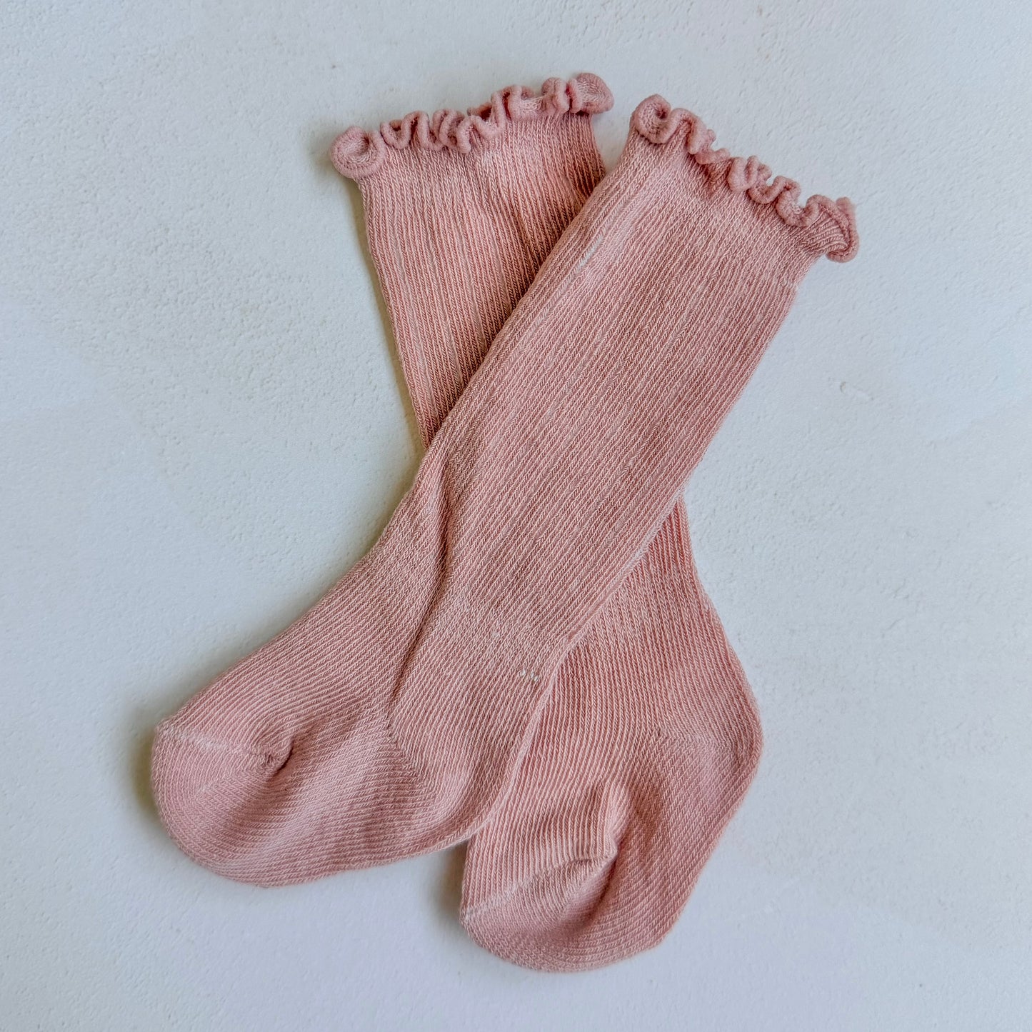 Pair of pink socks with ruffled top on a light gray background