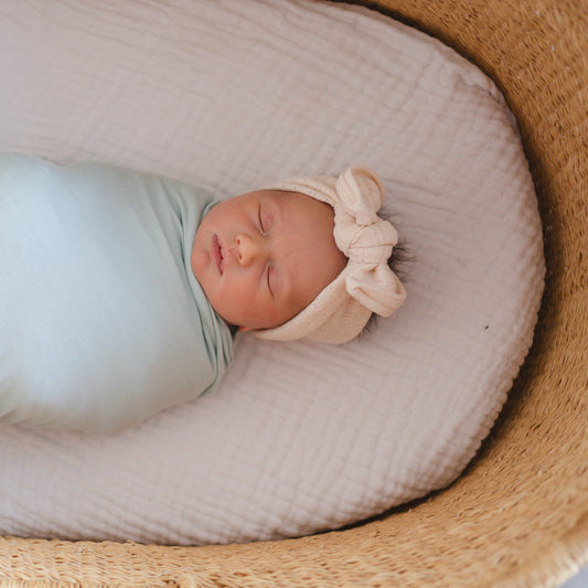 Newborn baby wrapped in a light blue blanket with a beige bow, lying in a woven basket.