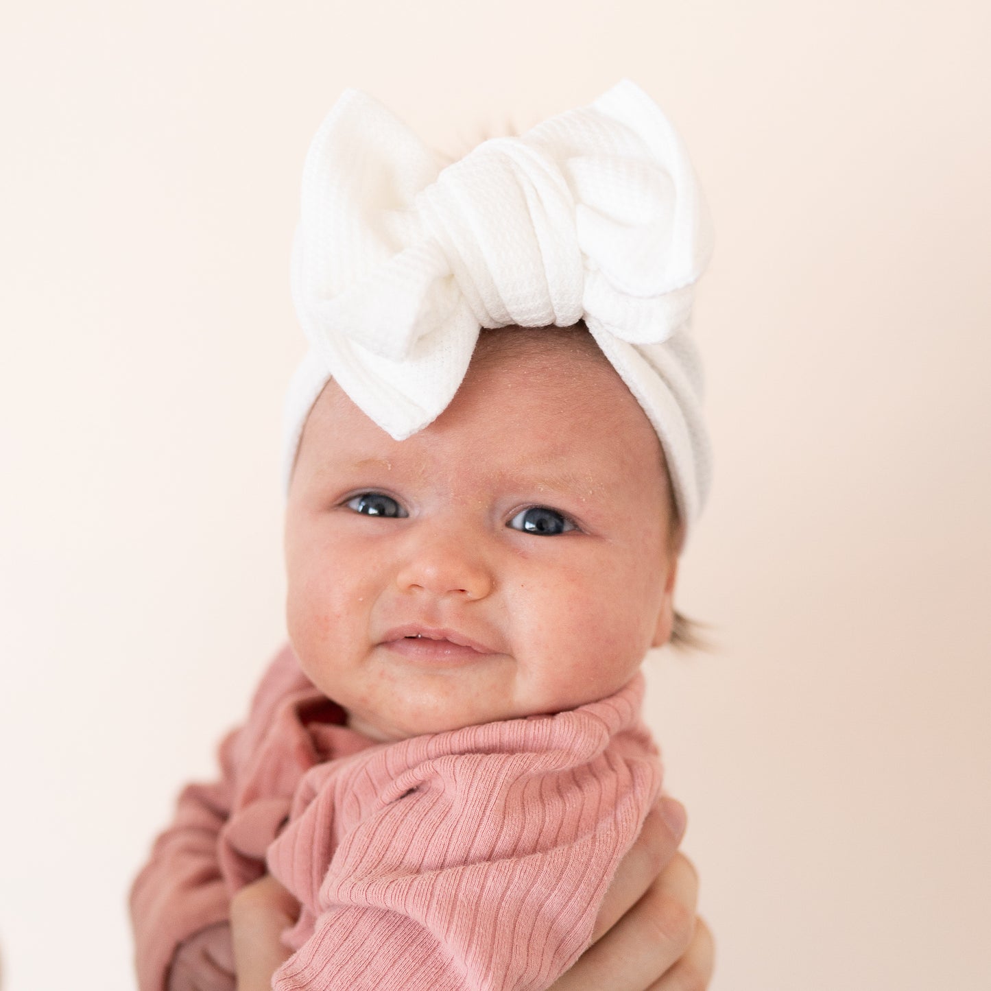 Baby wearing a white headband with a large bow on a beige background