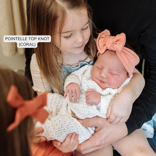 Top knot baby headband in coral, crafted from pointelle knit fabric, displayed on a white background