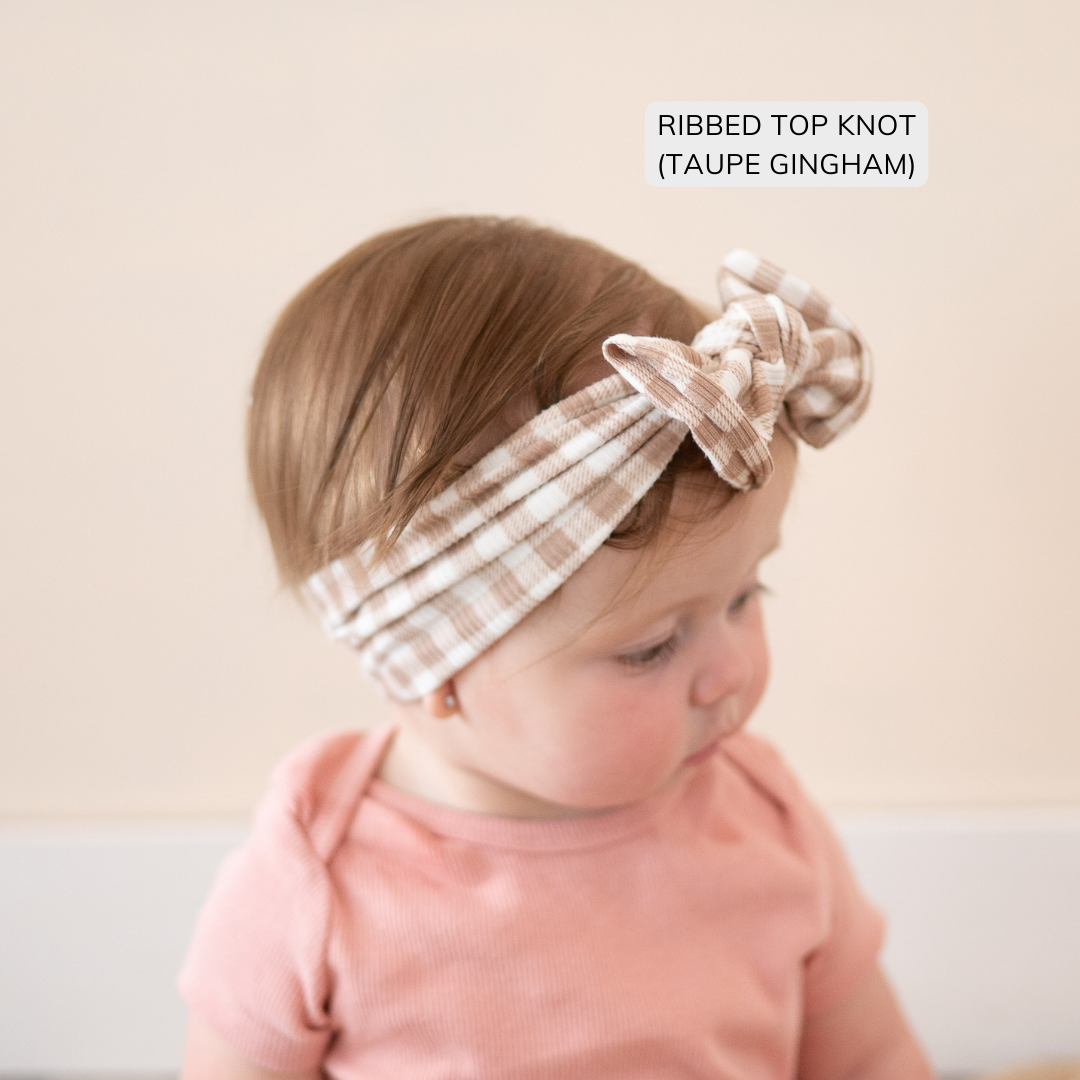 Baby wearing a ribbed top knot headband with gingham pattern on a plain background