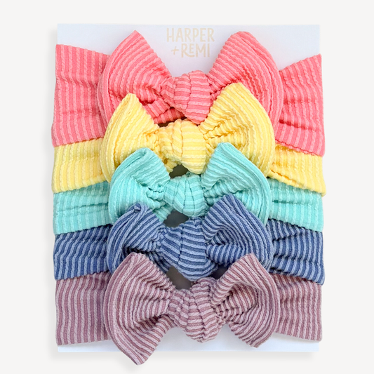 Hand holding a Harper + Remi branded card with colorful baby headbands in pink, yellow, aqua, blue and purple.