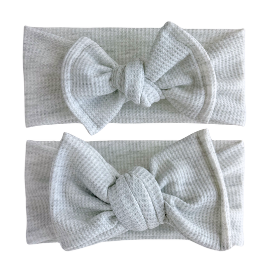 Two gray waffle knit headbands with large bows on a white background. Top is a top knot, bottom is an oversized bow.