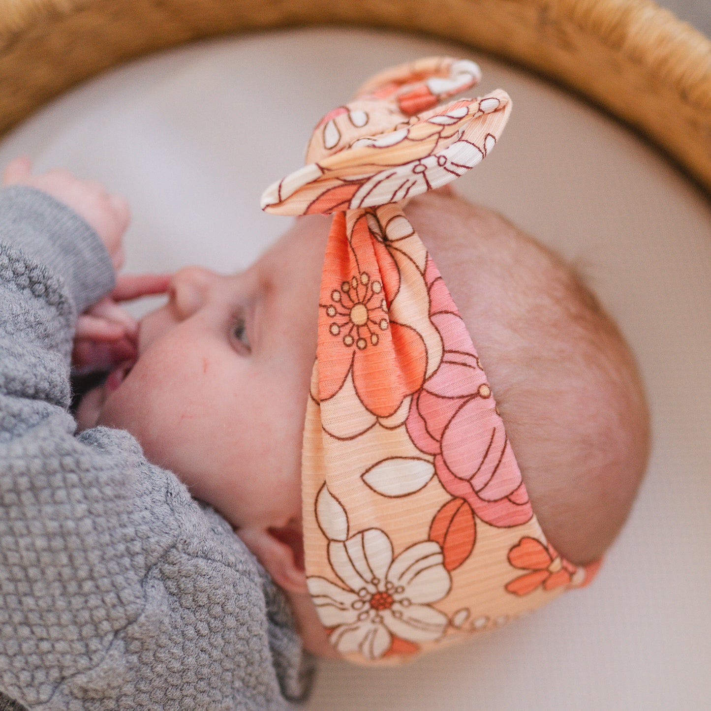 Baby wearing a coral floral top knot headband with a blurred background