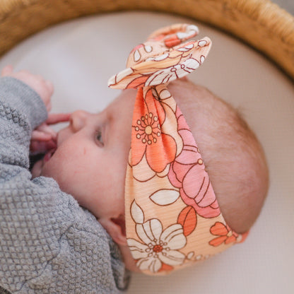 Baby wearing a coral floral top knot headband with a blurred background