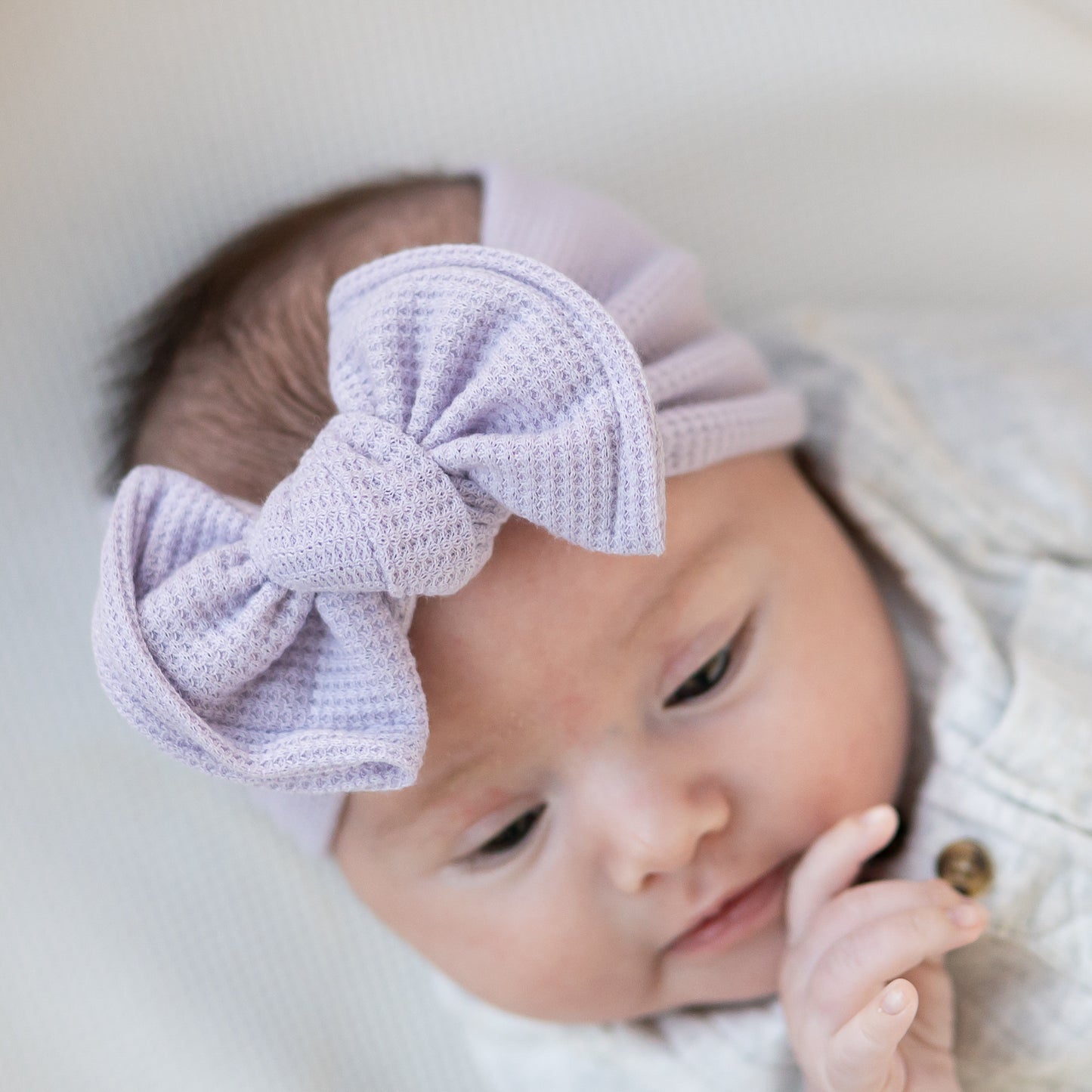 Baby wearing a lavender knit headband with a large bow on a light background
