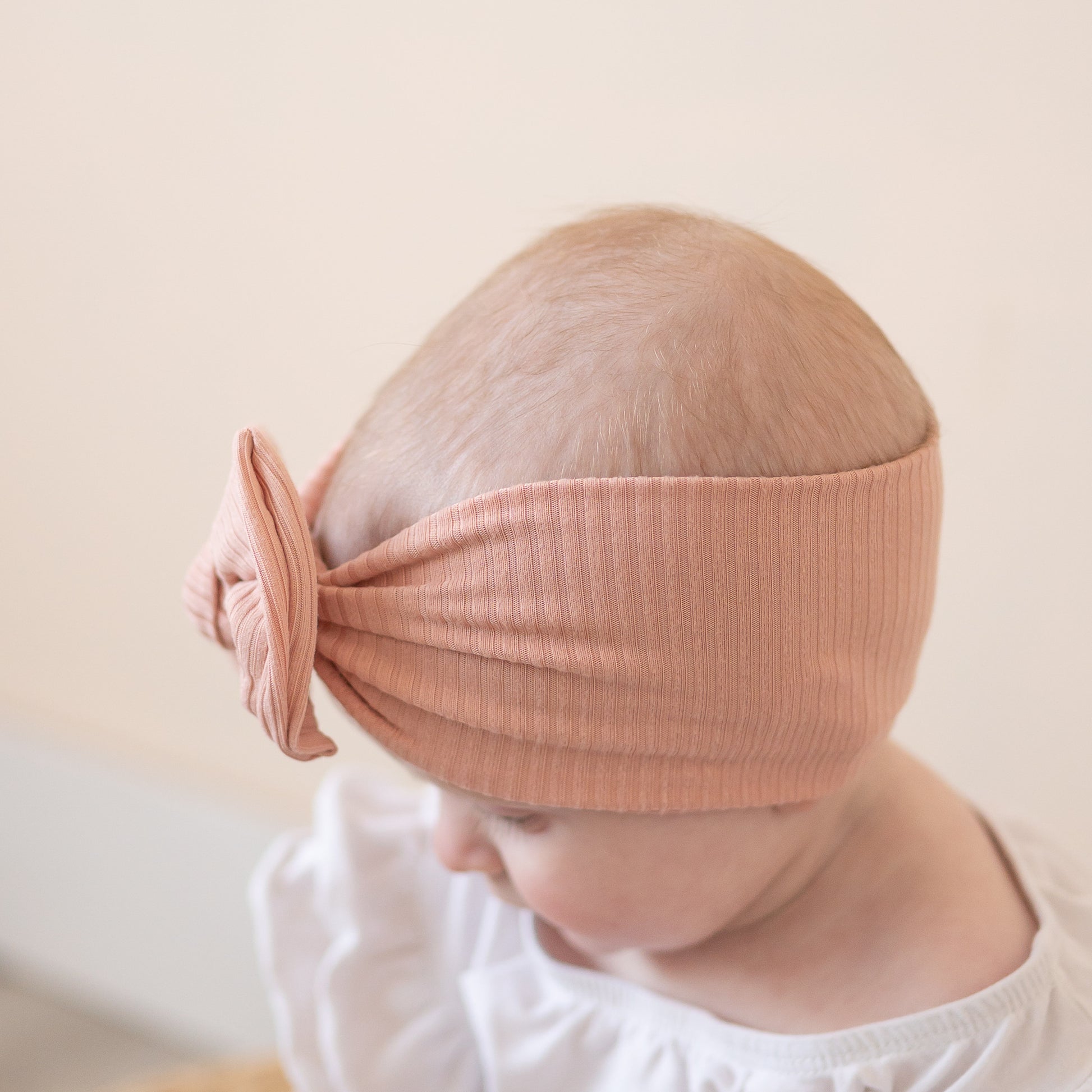 Baby wearing a dusty pink headband with a bow on a plain background