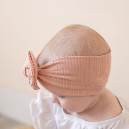 Baby wearing a dusty pink headband with a bow on a plain background