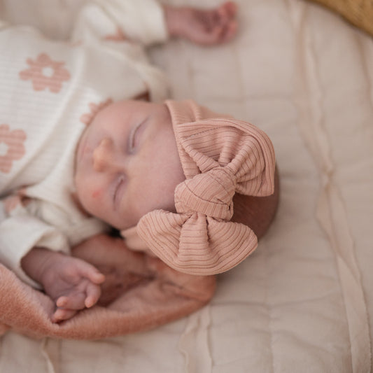 Newborn baby sleeping with a dusty pink ribbed knit top knot bow headband on a soft surface