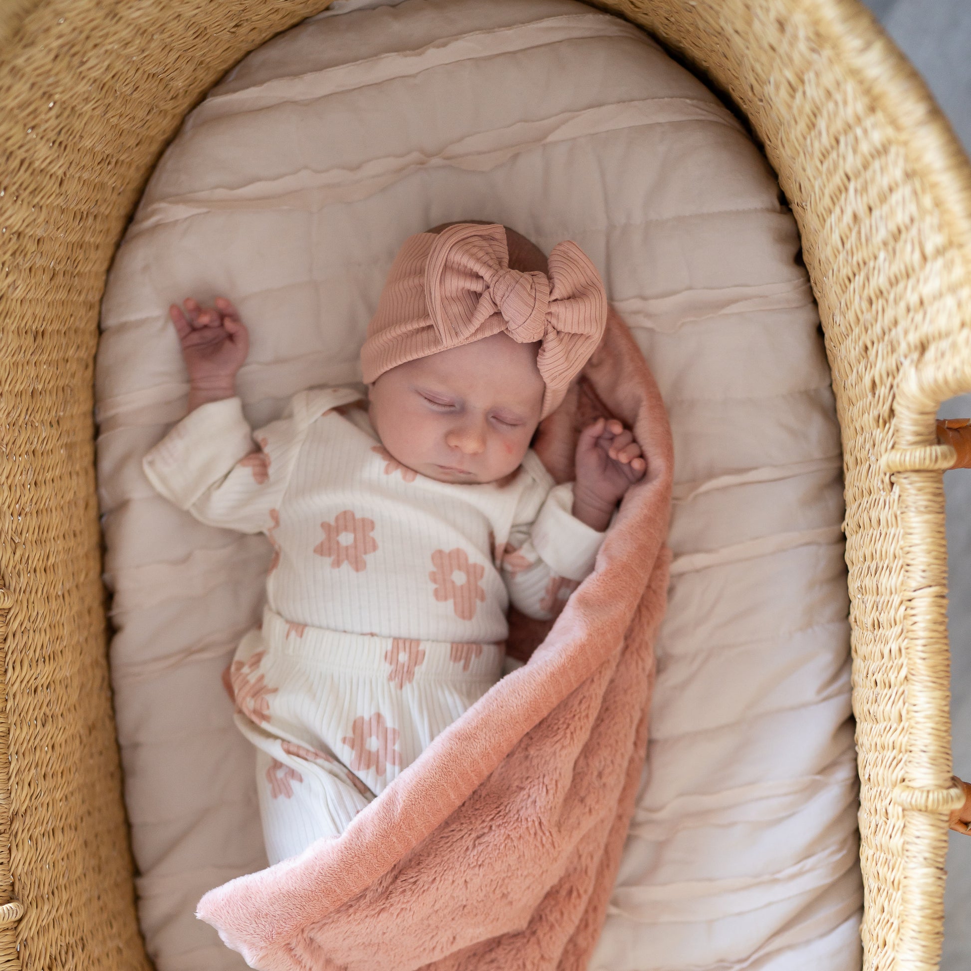 Newborn baby in a moses basket with a pink floral outfit and dusty pink ribbed headband.