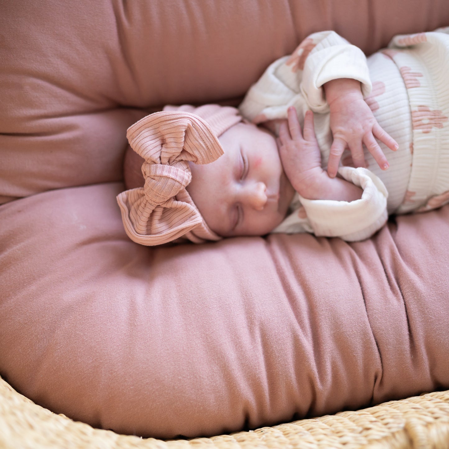 Newborn baby sleeping on a pink cushion with a dusty pink ribbed bow headband