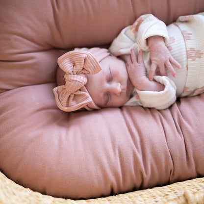 Newborn baby sleeping on a pink cushion with a dusty pink ribbed bow headband