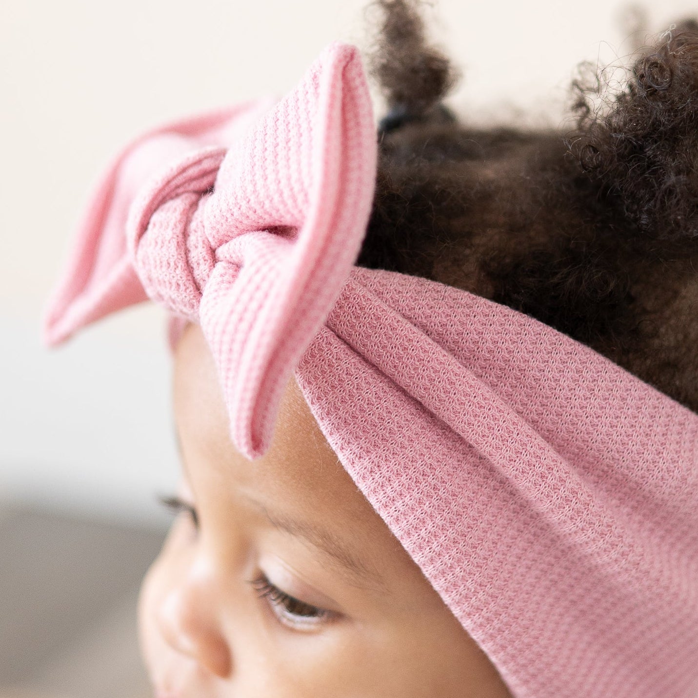 Close-up of a baby wearing a pink knotted headband with a blurred background