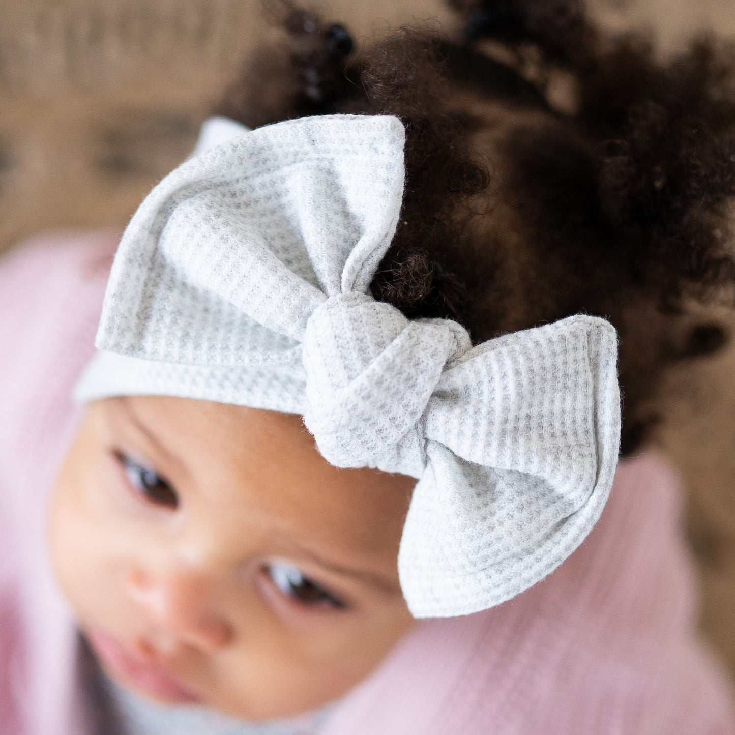 Detailed top view of a baby wearing a light gray waffle. textured headband with a bow on a blurred background