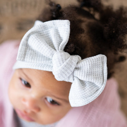 Detailed top view of a baby wearing a light gray waffle. textured headband with a bow on a blurred background