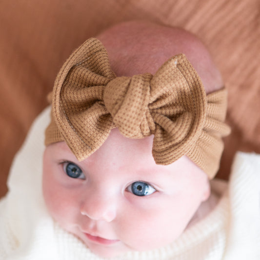 Top view of a baby wearing a brown waffle top knot bow headband with a blurred background