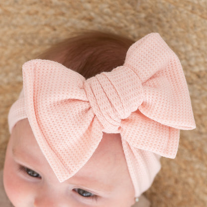 Detailed top view of a baby wearing a large pink waffle bow headband against a beige background