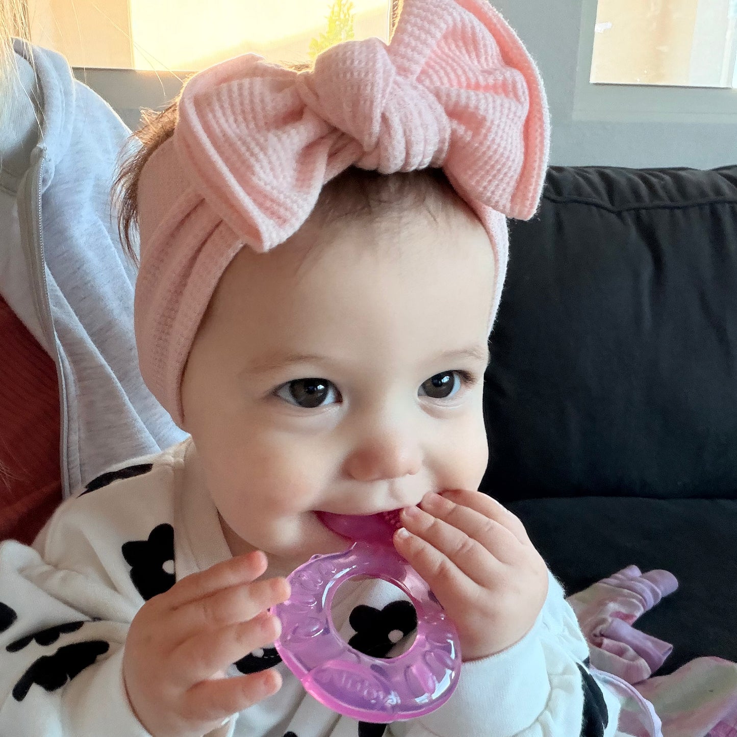 Baby wearing a pink headband with a bow, holding a purple teething ring.