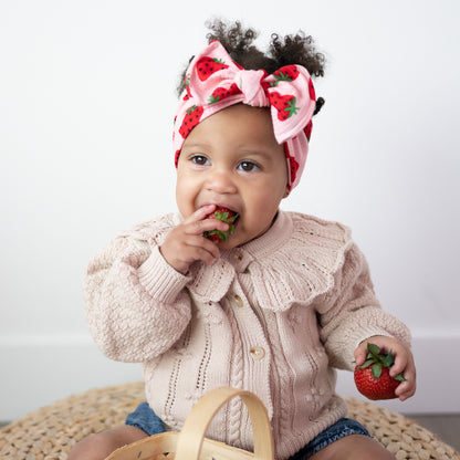 Baby wearing a strawberry-themed headband and eating strawberries.