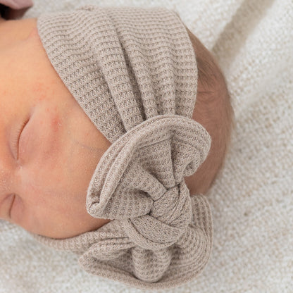 Detail top view of newborn baby wearing a taupe waffle textured headband on a soft beige background
