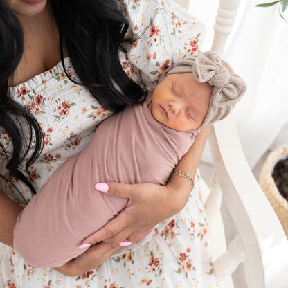 Woman holding a swaddled baby wearing a taupe waffle headband in a soft, indoor setting.