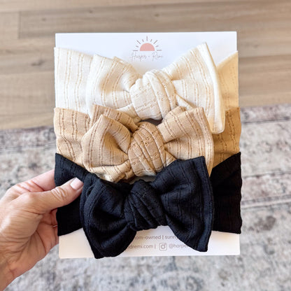 Set of beige and black headbands held over a branded card with a wooden surface background.