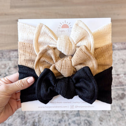 Set of beige and black headbands with bow designs held against a white card.