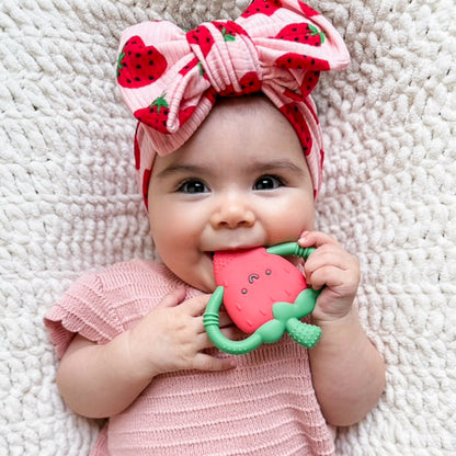 Top knot baby headband in light pink with red strawberry pattern, crafted from ribbed knit fabric, displayed on a white background