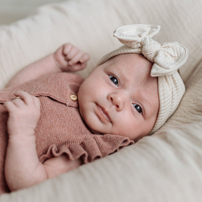 Newborn baby wearing a beige ribbed top knot bow.