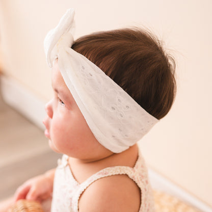 Side view of a baby wearing a white eyelet lace top knot bow.