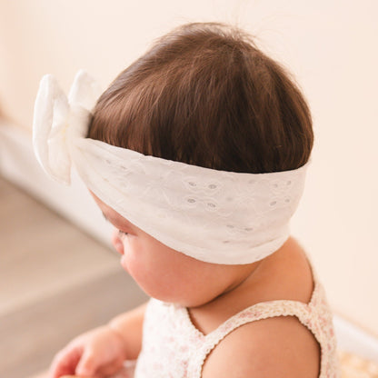 Baby wearing a white headband with a bow on a neutral background