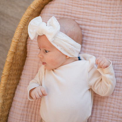 Baby in Moses basket looking to the side, wearing a white eyelet top knot headband.