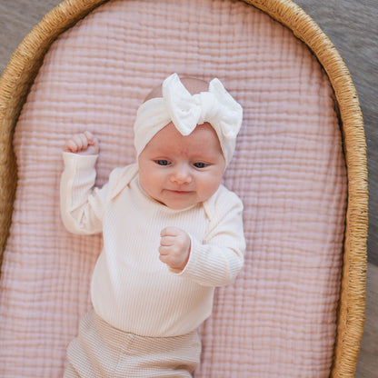Newborn baby smiling, wearing a white eyelet top knot.
