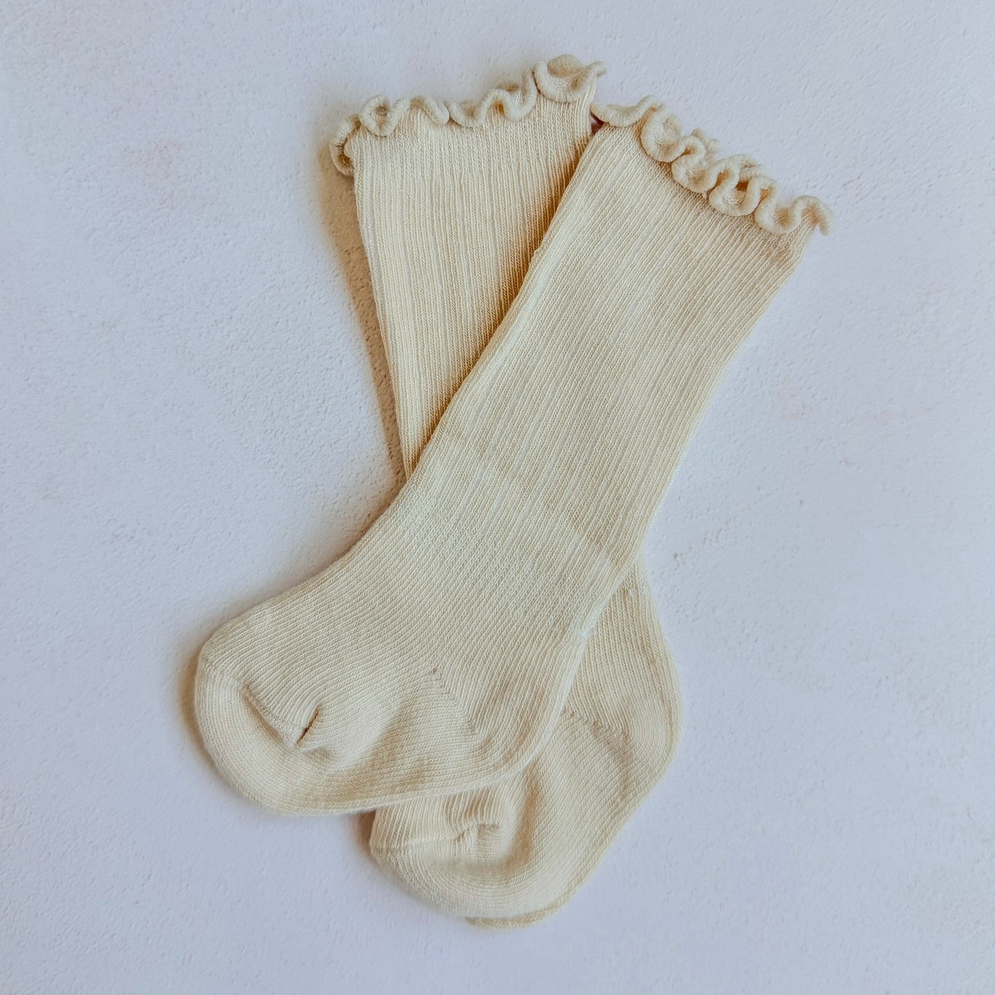 Pair of beige knee socks with ruffled top on a light gray background