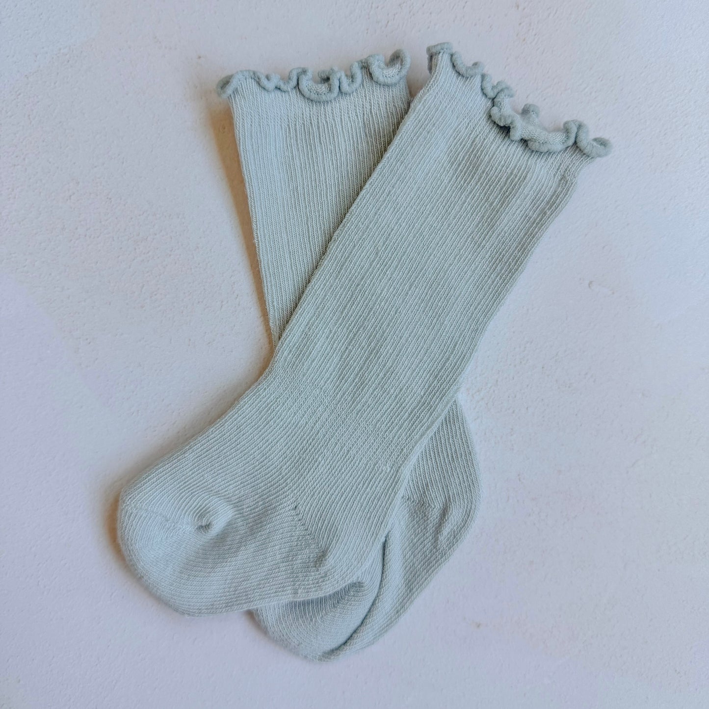 Pair of light gray ribbed socks with ruffled cuffs on a white background
