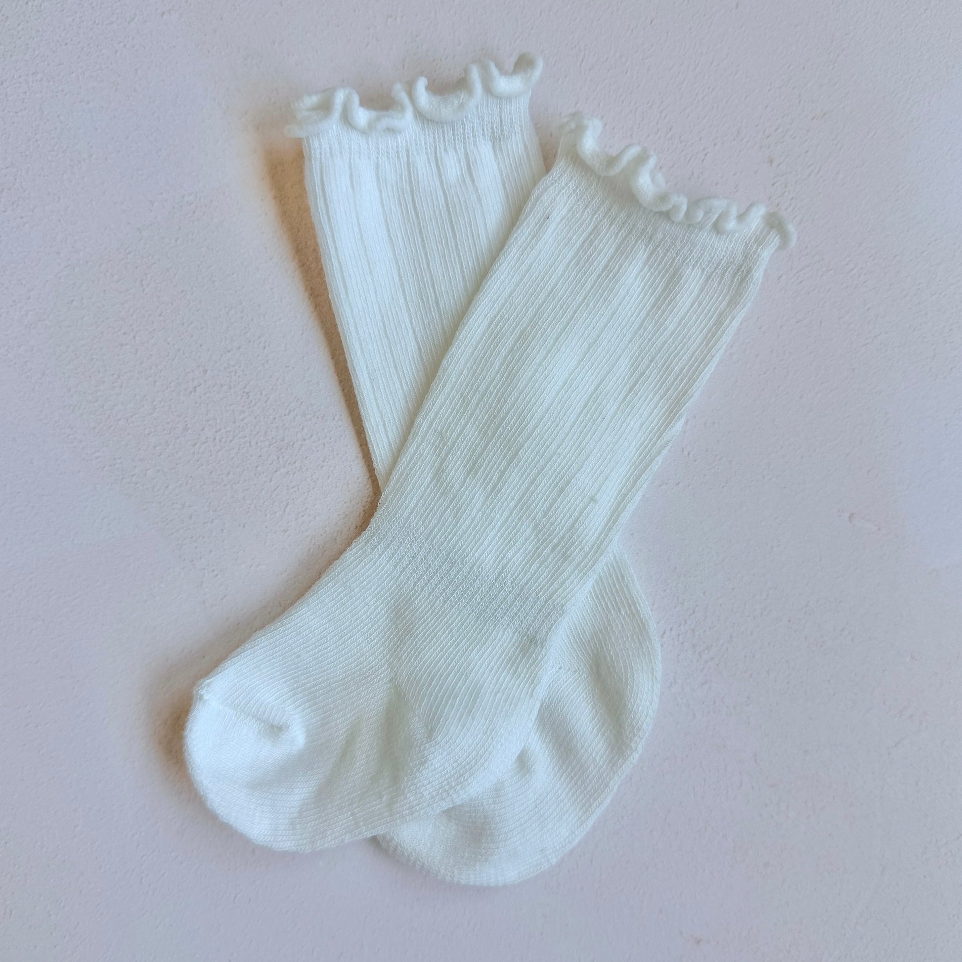 Pair of white socks with lace trim on a light pink background