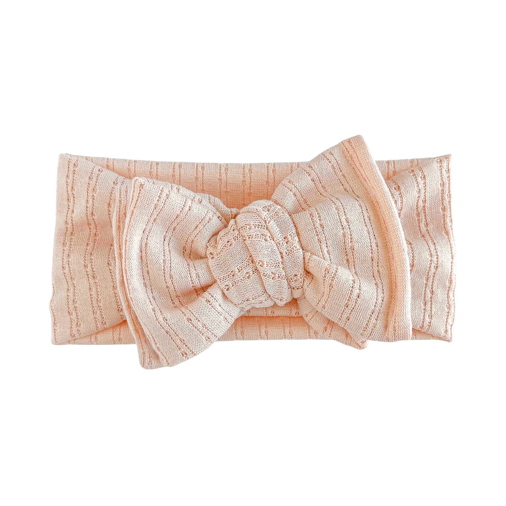 Top knot baby headband in blush (nude pink), crafted from pointelle knit fabric, displayed on a white background