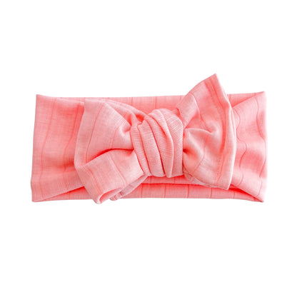 Top knot baby headband in bright coral, crafted from wide ribbed knit fabric, displayed on a white background