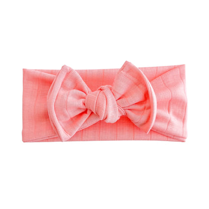 Oversized bow baby headband in bright coral, crafted from wide ribbed knit fabric, displayed on a white background