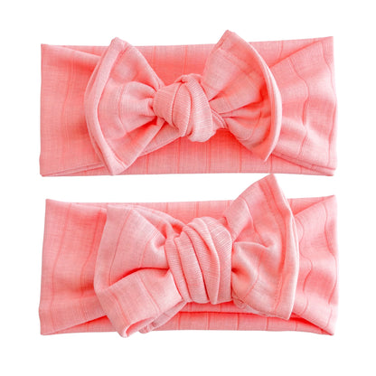 Baby girl headbands in top knot and oversized bow styles in bright coral, made from wide ribbed knit fabric