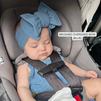 Baby sleeping in a car seat wearing a blue oversized bow headband.