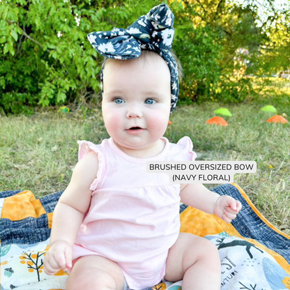 baby sitting on a blanket in the grass, wearing a blue floral oversized bow headband