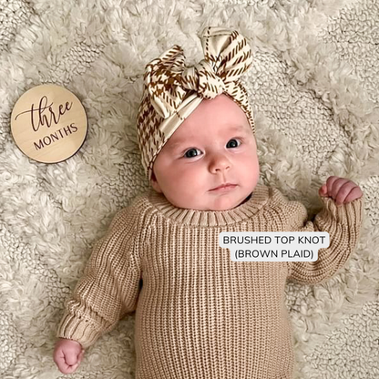 3 month old baby wearing cream and brown plaid top knot bow and a light brown sweater.