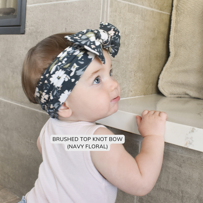 Baby wearing a navy blue floral top knot headband, looking to the side.