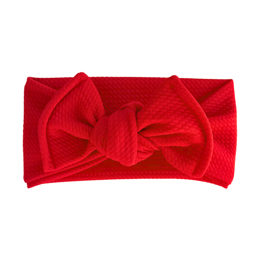 A bright red textured fabric headband with a large bow detail, shown flat against a solid white background.