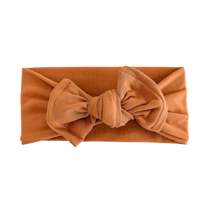 Top knot bow baby headband in burnt orange, crafted from double brushed knit fabric, displayed on a white background