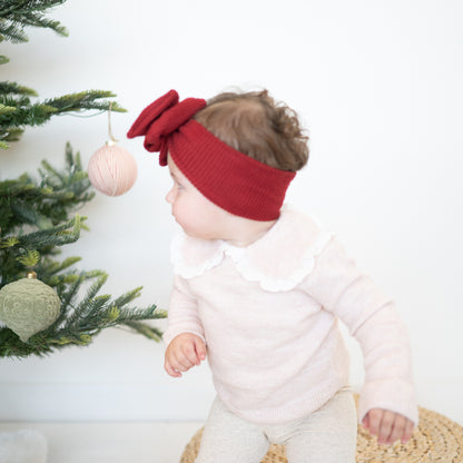 Baby wearing a red headband with a Christmas tree and ornaments in the background