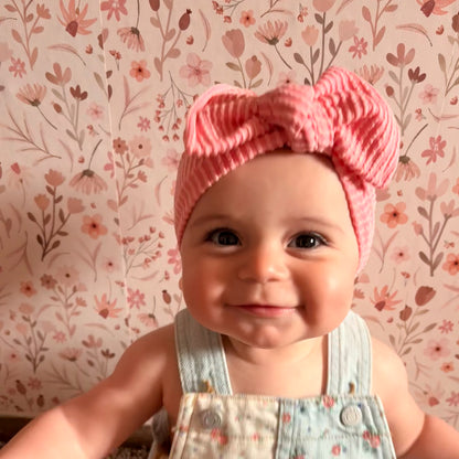 Baby wearing a pink knitted headband with a floral patterned wallpaper in the background